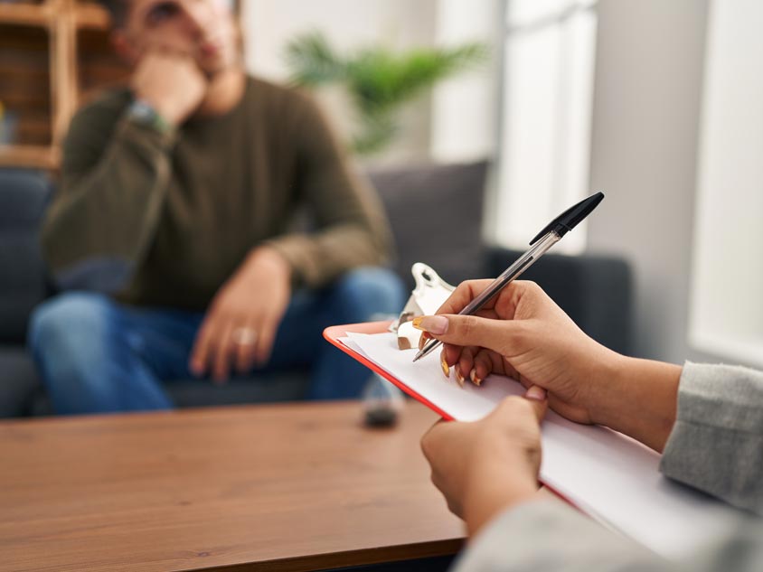 A mental health professional checking a clipboard while a patient sits down